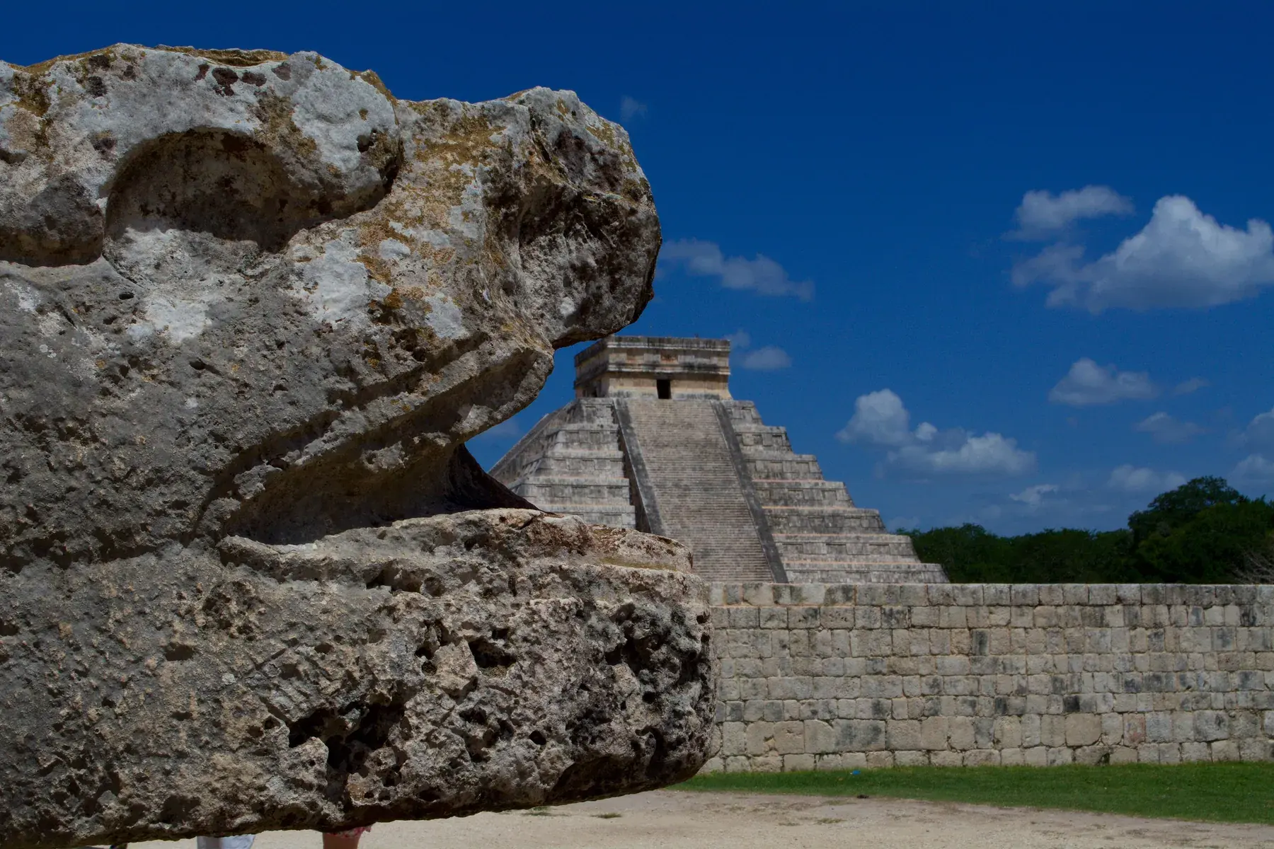 Feathered serpent head carved in stone, with the El Castillo pyramid in the background