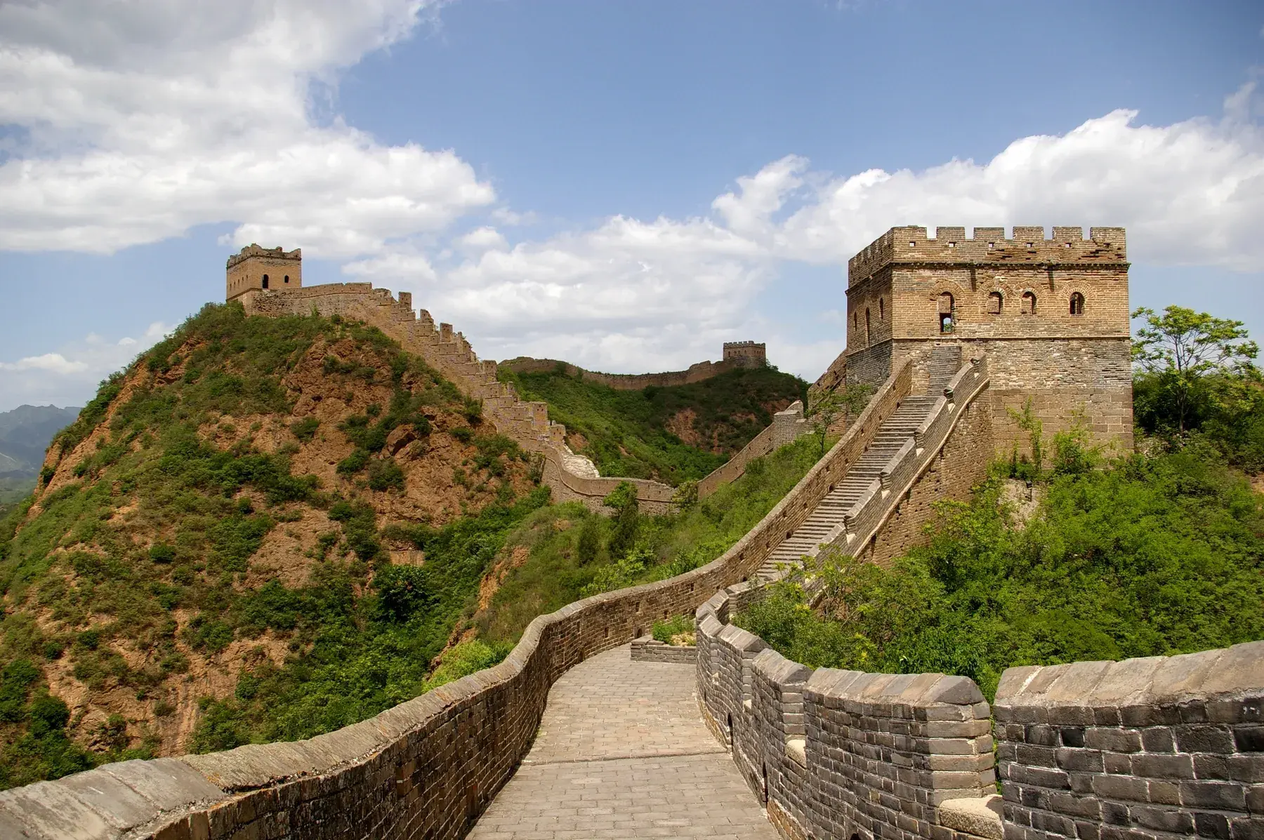 Stone walkway with battlements on the Great Wall of China leading to a watchtower, under a cloudy sky