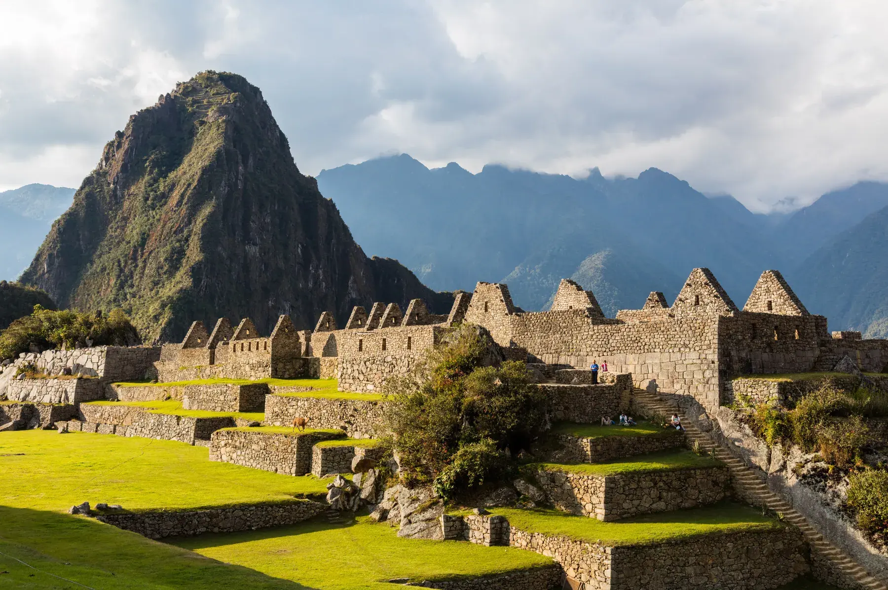 Ruins and lawns of Machu Picchu with Huayna Picchu peak and mountains under clouds in the background
