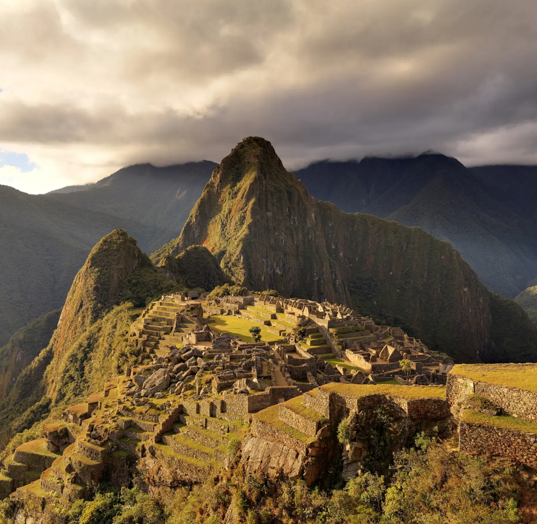 Machu Picchu at twilight, with golden light on the ruins, Huayna Picchu, and clouds over the Andes
