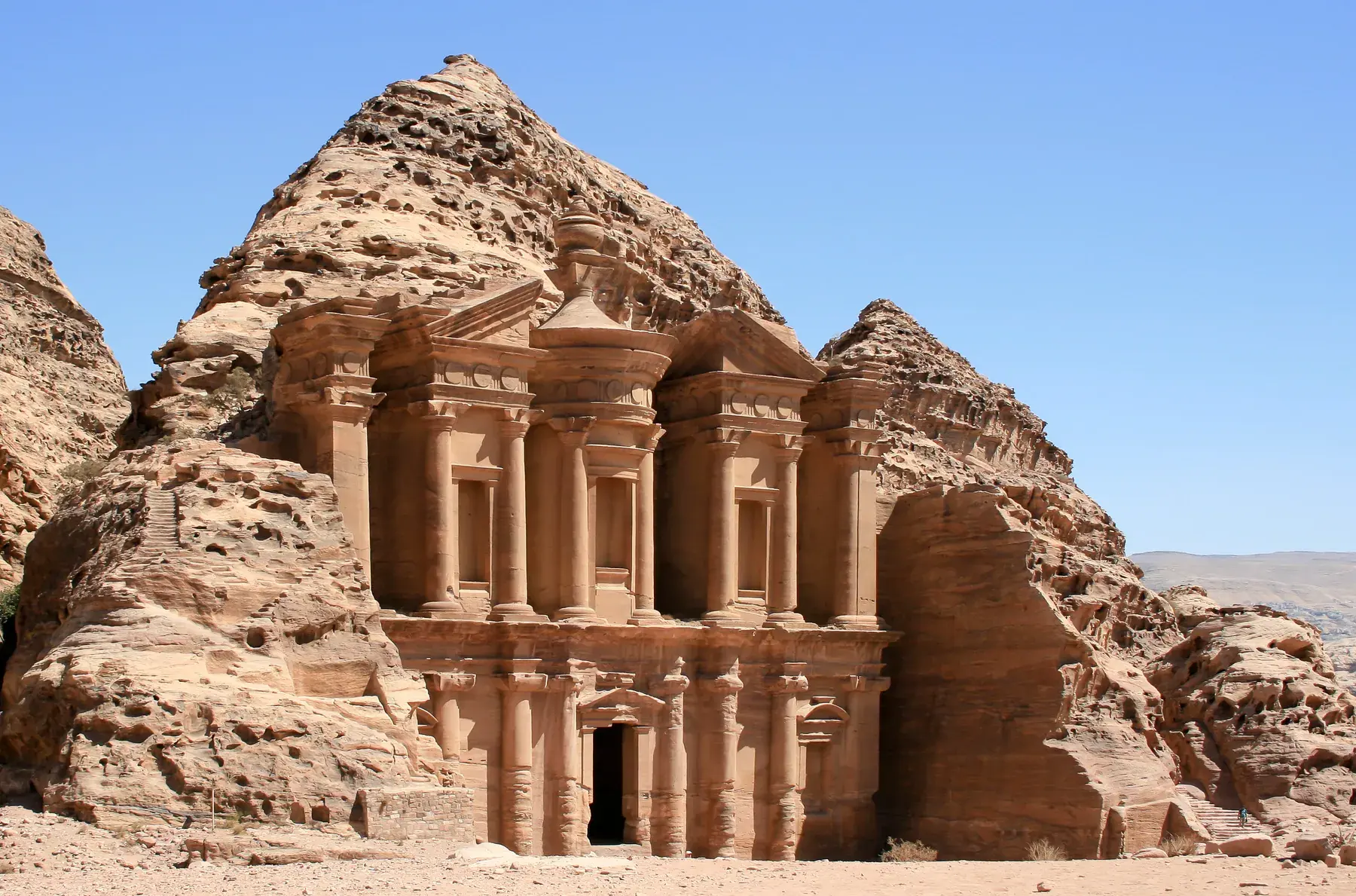 Monumental facade of the Monastery (Ad Deir), carved into the rock of Petra’s mountains under a blue sky