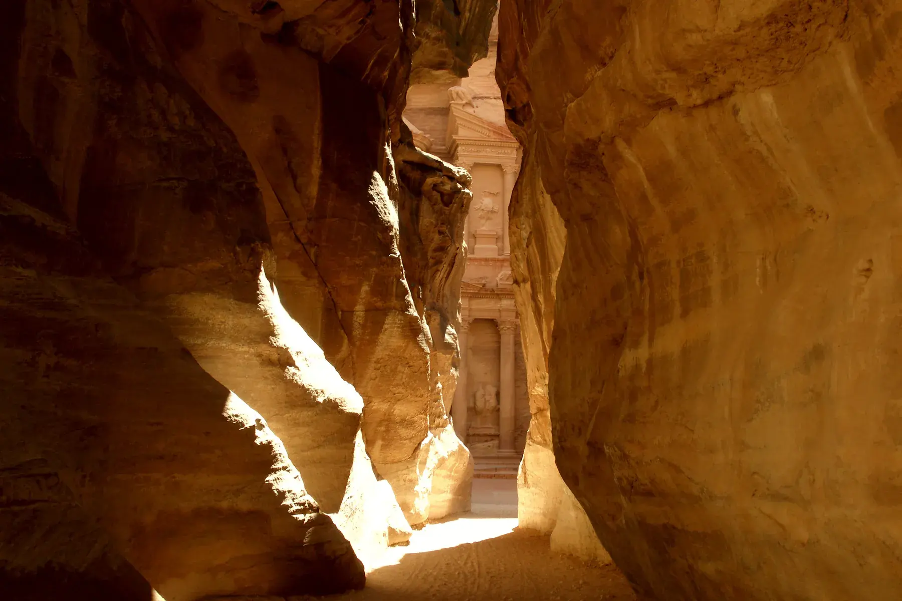 Golden cliff walls of the Siq, Petra’s narrow entrance canyon, revealing the facade of the Treasury in the background