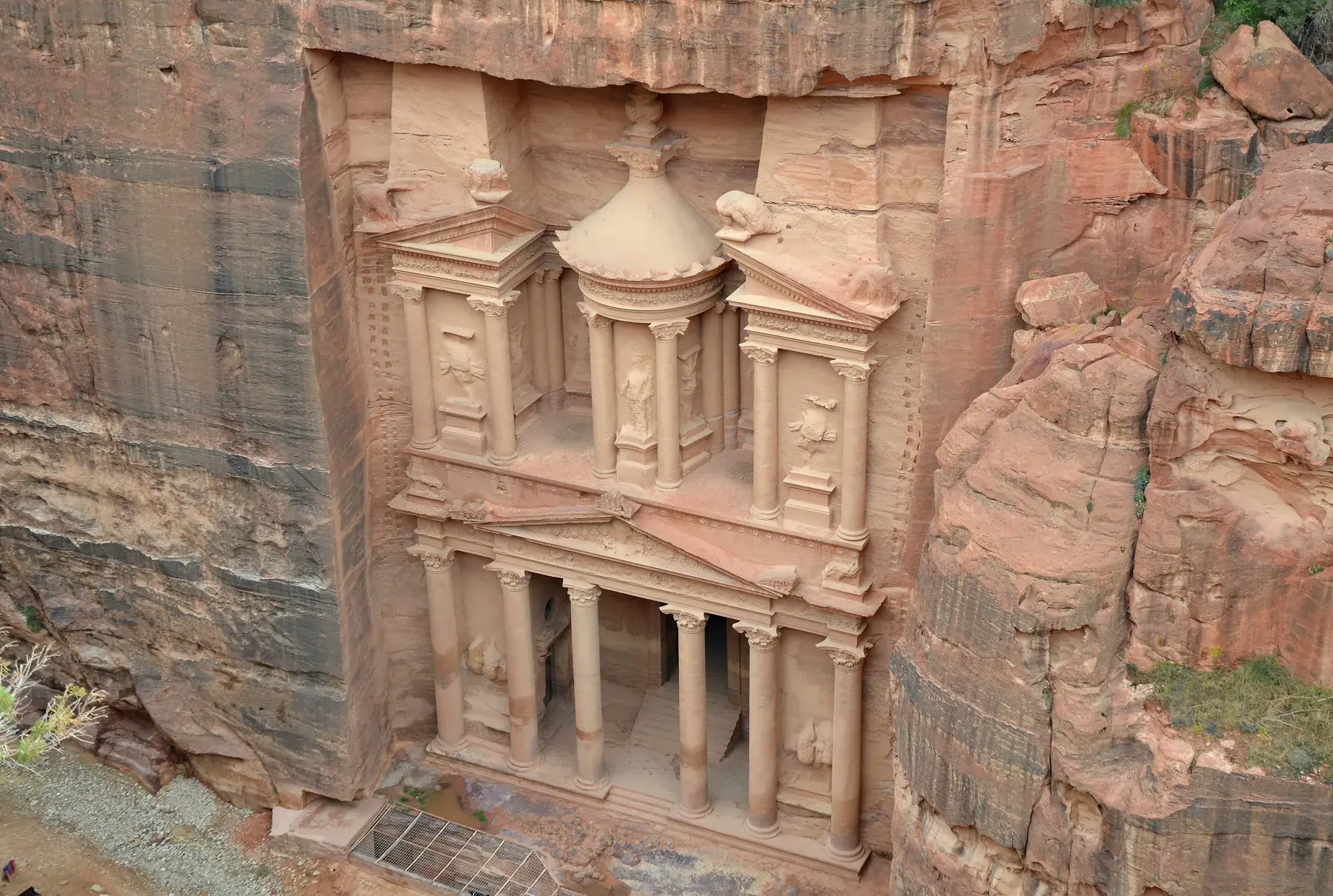 View from above of the facade of the Treasury (Al-Khazneh), surrounded by sandstone cliff walls in Petra