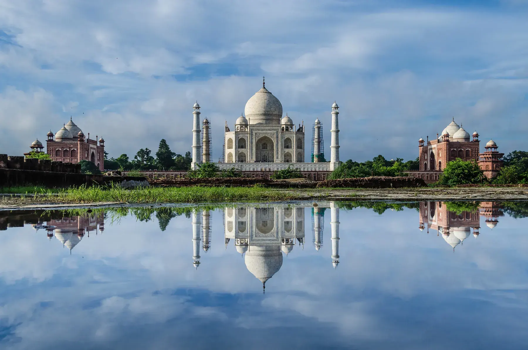 Taj Mahal and its red sandstone buildings reflected in the waters of the Yamuna River, seen from the opposite bank