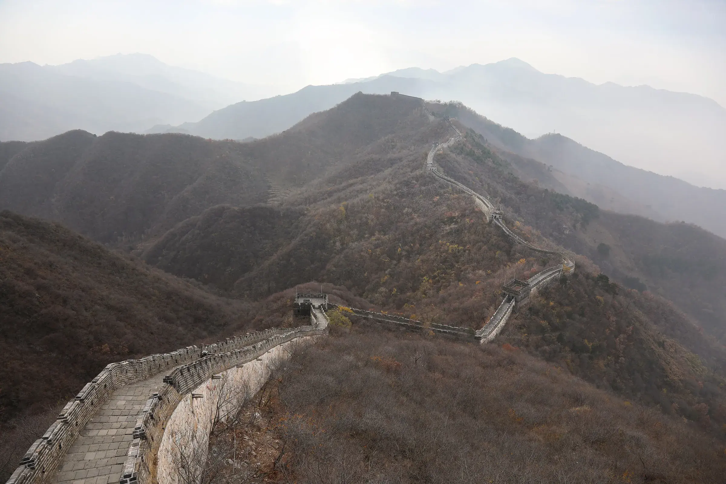Great Wall of China at Mutianyu crossing mist-shrouded mountains, with autumn foliage